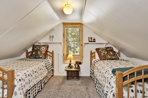 A cozy attic bedroom with two wooden beds, a small table with a lamp, and a window with a view of trees. - Moonridge R N R #2320 (Big Bear Lake)