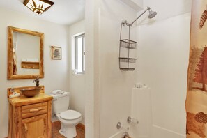 A bathroom with a wooden vanity, a white toilet, a shower with a metal rack, and a mirror with a picture frame. - Moonridge R N R #2320 (Big Bear Lake)