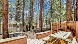 A wooden deck with benches and a picnic table, surrounded by tall pine trees. - Moonridge R N R #2320 (Big Bear Lake)