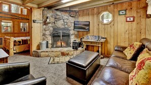 A cozy cabin interior with a stone fireplace, wooden walls, a television, and a comfortable seating area. - Moonridge R N R #2320 (Big Bear Lake)