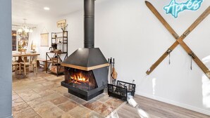 A modern living room with a wood-burning stove, a dining area with a wooden table and chairs, and a wall-mounted neon sign. - Apres Chalet #2364 (Sugarloaf)