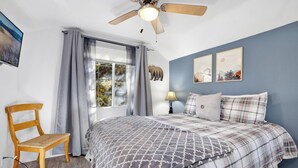 A bedroom with a bed, a chair, a ceiling fan, a window with curtains, and wall art. - Apres Chalet #2364 (Sugarloaf)