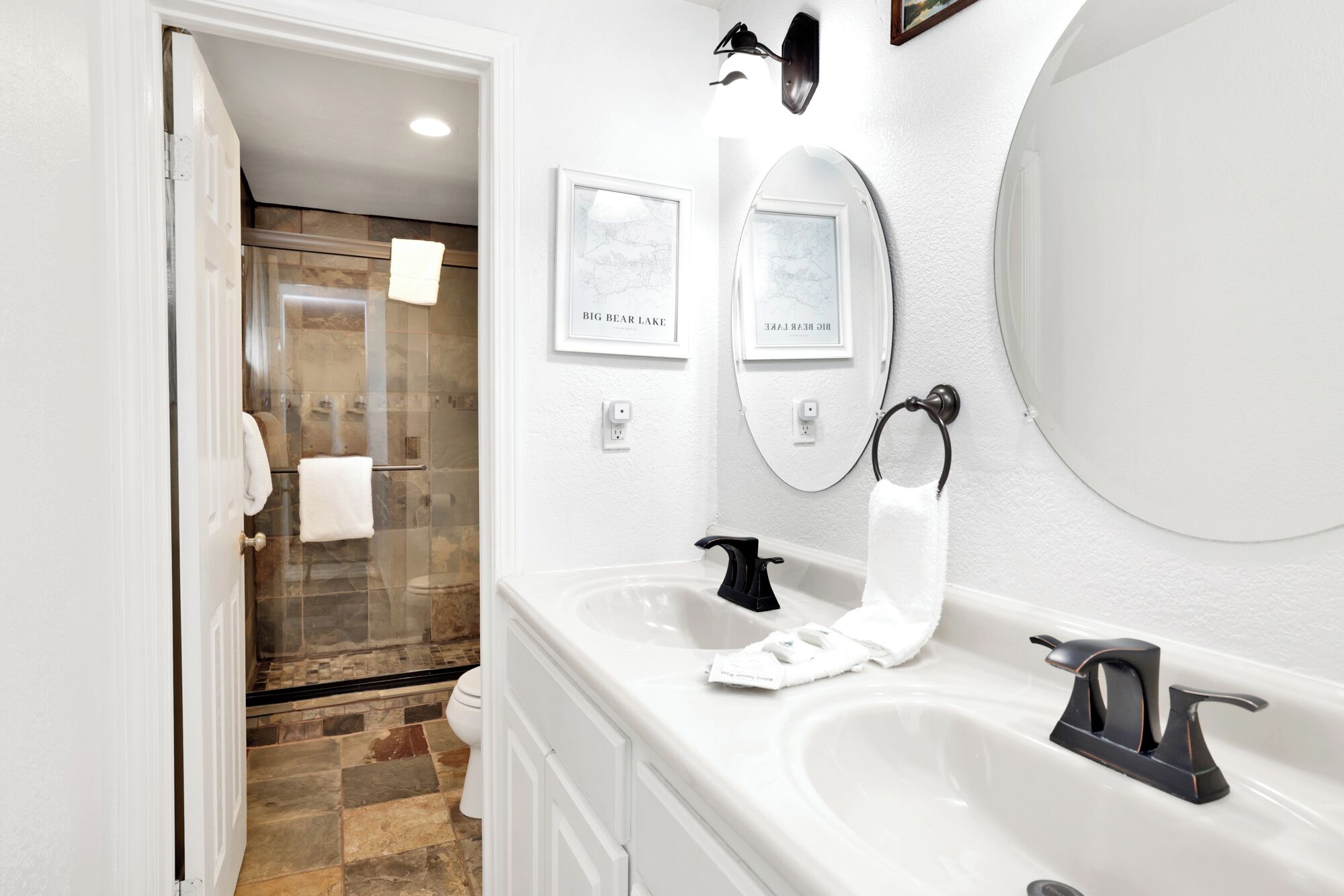 Un baño moderno con un espejo grande, dos lavamanos y una zona de ducha.