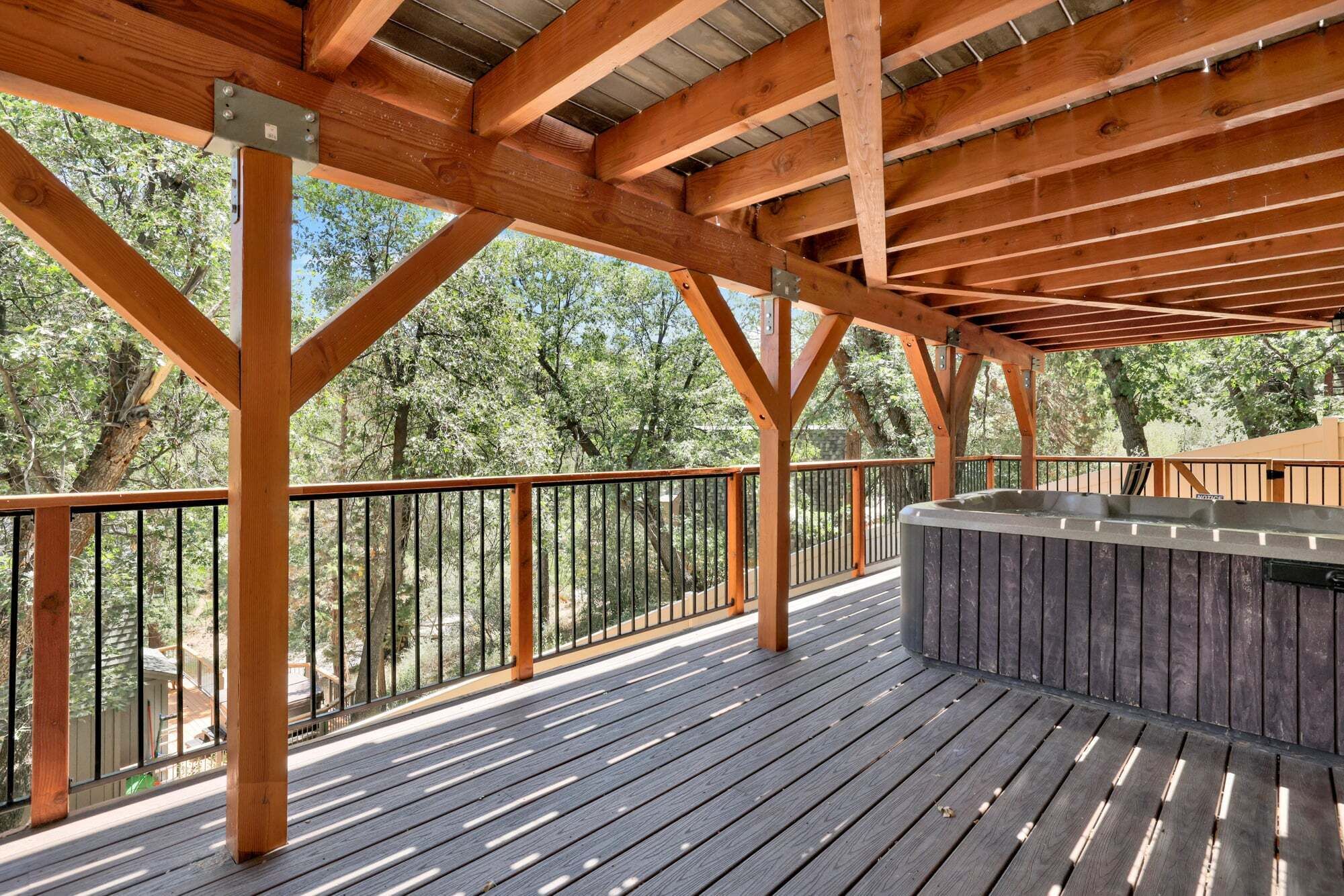 A wooden deck with a hot tub, metal railings, and trees in the background.