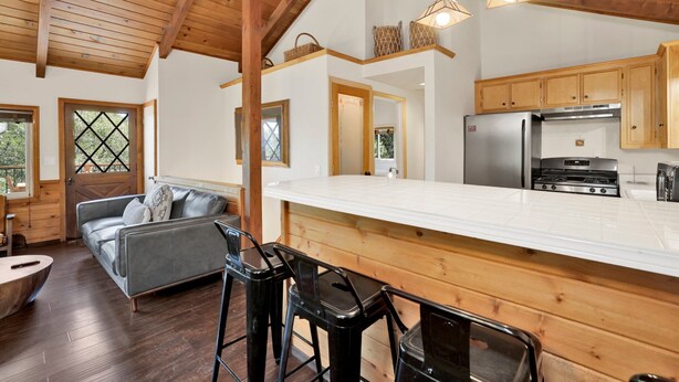A modern kitchen with wooden cabinets, a stainless steel refrigerator, and a large island. - Black OAK Cabin #1977 (Big Bear City)