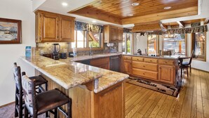A spacious kitchen with wooden cabinets, a granite countertop, and a large island. - Cove Lakefront Chalet #2098 (Big Bear Lake)