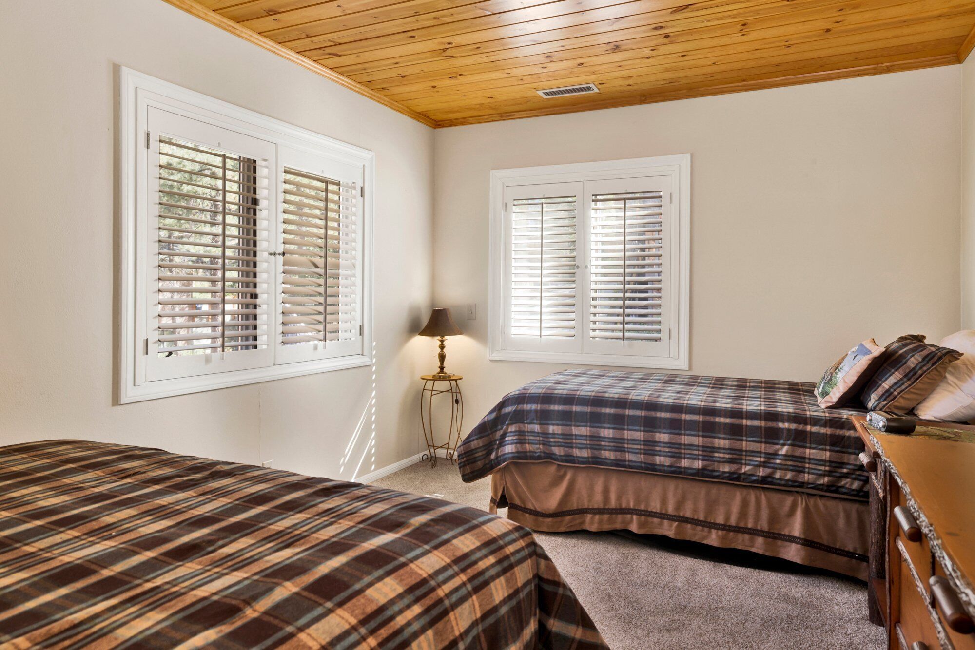 A bedroom with two beds, wooden ceiling, and windows with blinds.