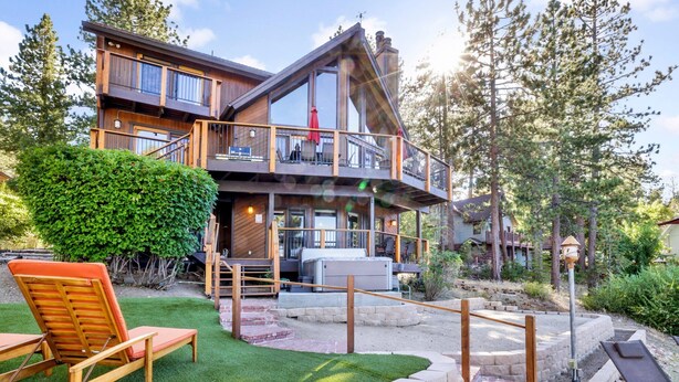 A two-story wooden house with a balcony, a patio with a lounge chair, and a well-maintained garden. - Cove Lakefront Chalet #2098 (Big Bear Lake)