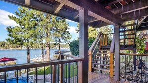 A wooden deck with a hot tub, outdoor seating, and a view of a lake. - Cove Lakefront Chalet #2098 (Big Bear Lake)
