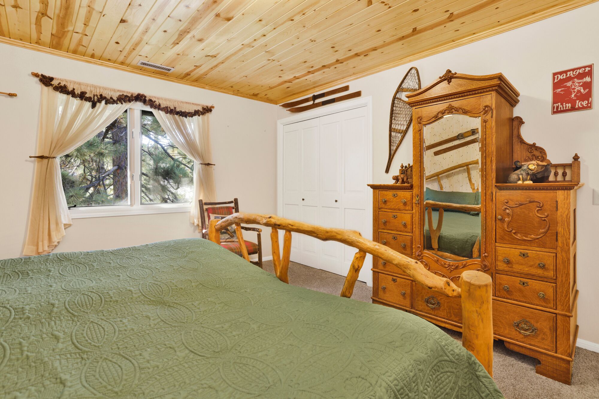A bedroom with a wooden bed frame, a wooden dresser with a mirror, and a window with curtains.