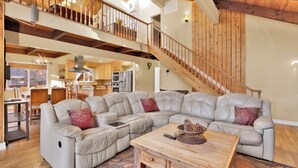 Un vaste espace de vie comprenant un grand canapé d’angle, une table basse en bois et un escalier menant à l’étage supérieur.