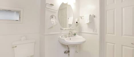 A bathroom with a pedestal sink, a toilet, a mirror, and a towel rack.