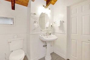 A bathroom with a pedestal sink, a toilet, a mirror, and a towel rack. - The Cozy Cottage#2384 (Big Bear City)