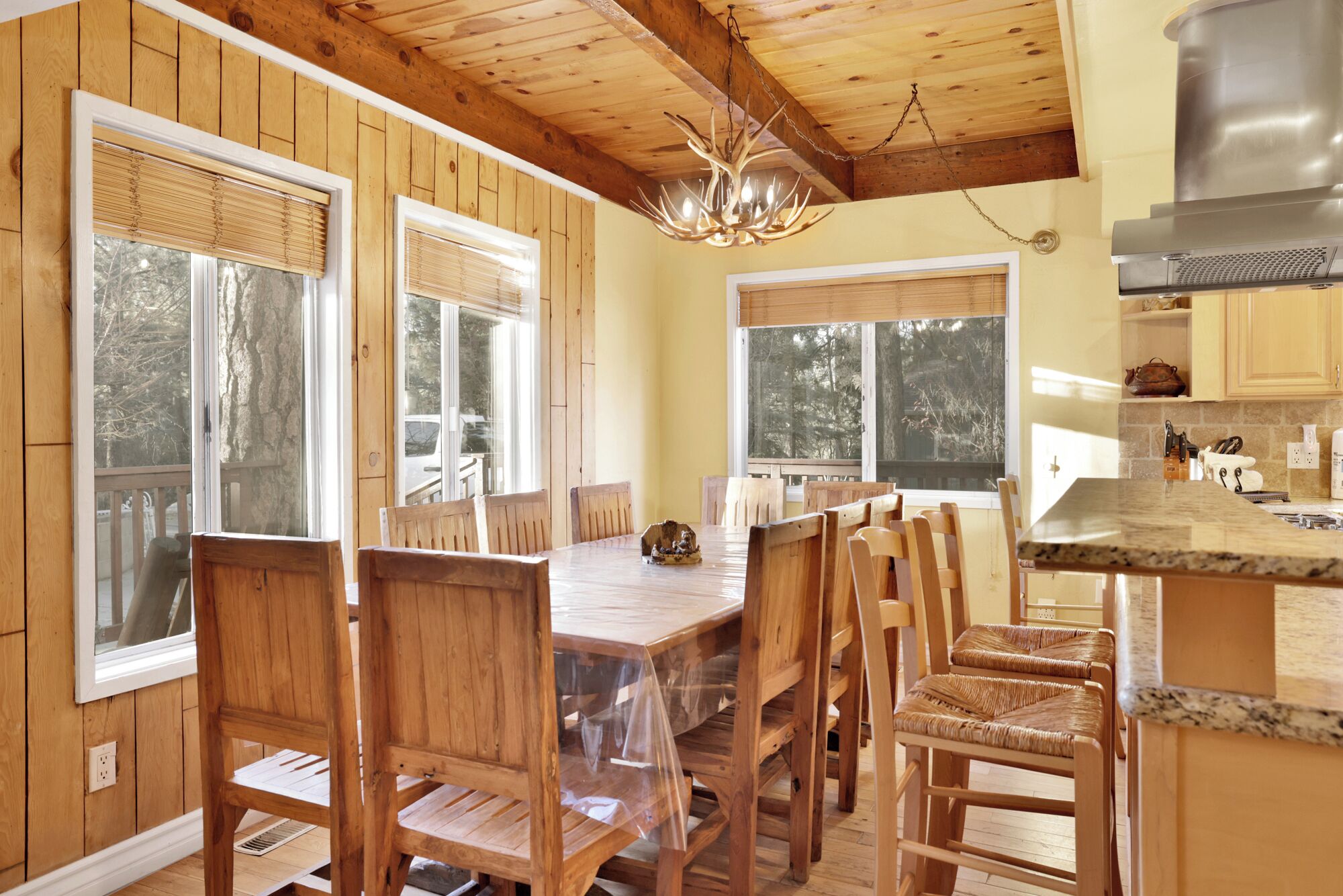 A wooden dining area with a large table and chairs, a chandelier, and a kitchen area with a stainless steel range hood.