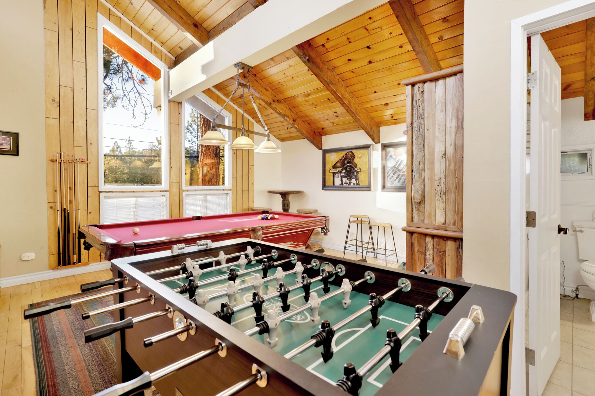 A room with a foosball table, pool table, and a bar area.