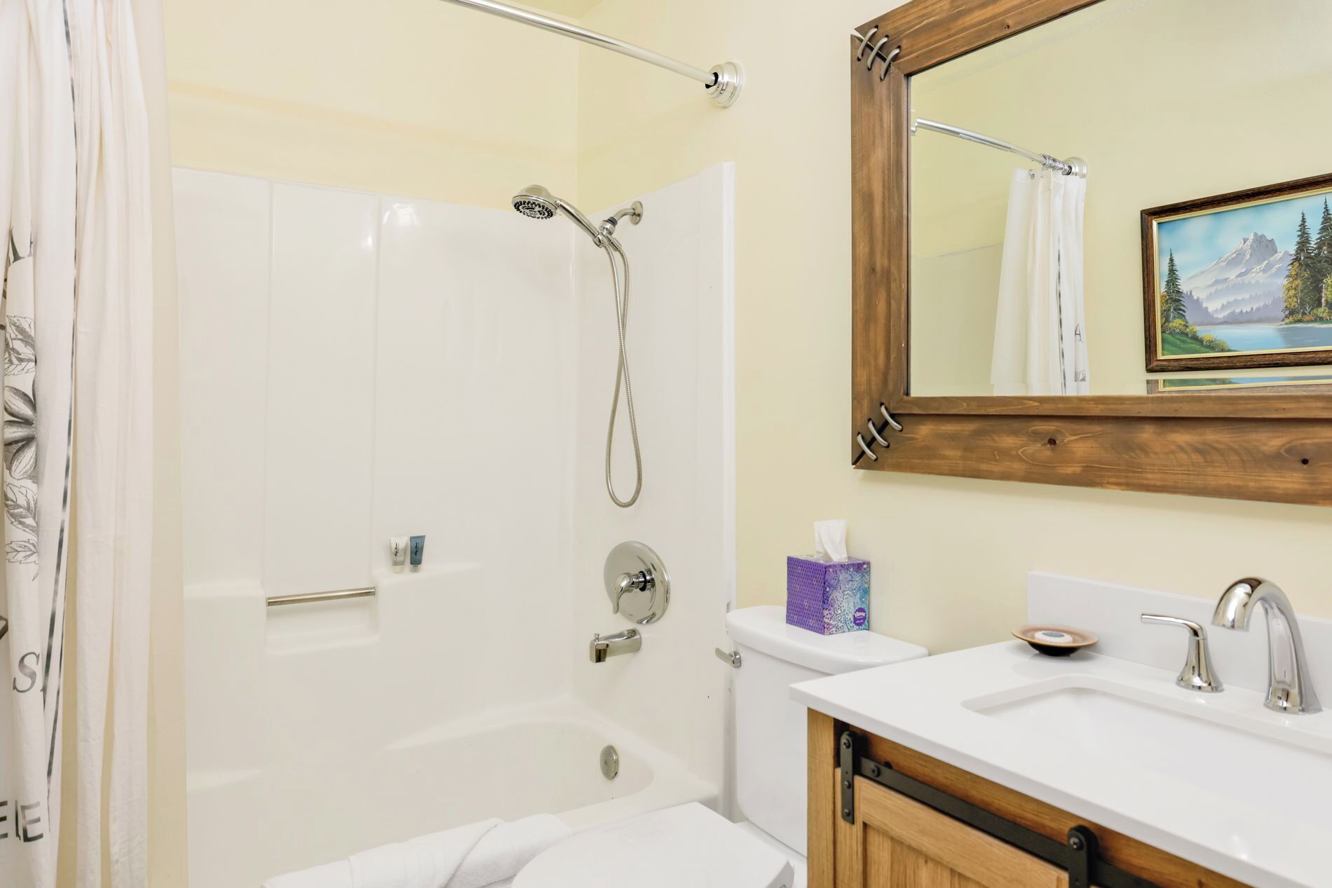 Une salle de bain équipée d’une douche, de toilettes, d’un lavabo et d’un miroir agrémenté d’un tableau.