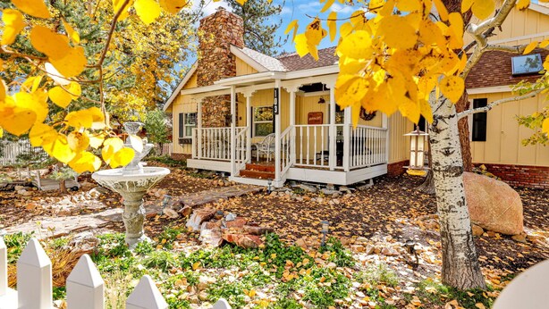 A house with a stone chimney, a porch with white railings, and a yard with fallen leaves. - THE Winding Lane House EST 1932 #2360 (Big Bear City)
