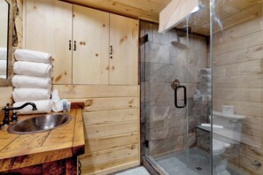 A wooden cabin bathroom with a glass shower enclosure, a sink, and neatly stacked towels. - Top Notch Lodge#2056 (Big Bear Lake)