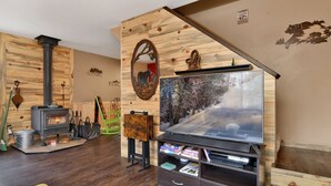 A cozy room with a wood-burning stove, a television, and a bookshelf. - Emma's Cottage#2267 (Big Bear City)