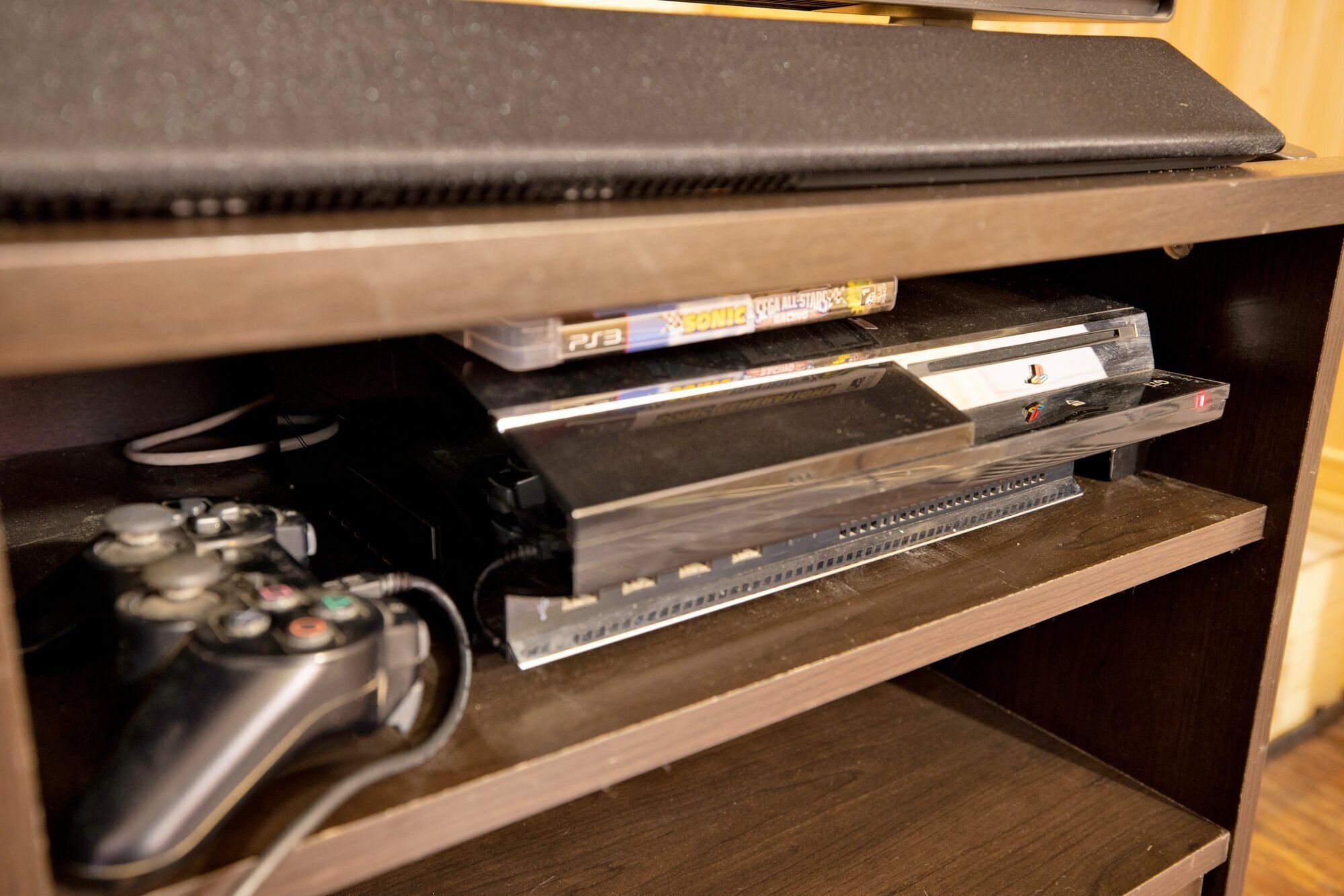 A wooden entertainment center with a PlayStation console, controller, and a DVD player.
