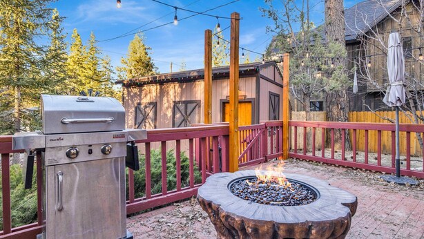 An outdoor patio with a Char-Broil grill, a fire pit, and a wooden deck with a red railing. - Emma's Cottage#2267 (Big Bear City)
