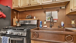 A kitchen with a stainless steel stove, wooden cabinets, a textured backsplash, and a sink with a faucet. - Emma's Cottage#2267 (Big Bear City)