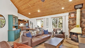 A cozy living room with a fireplace, wooden ceiling, and a view of the outdoors.