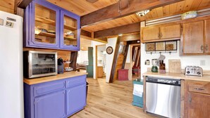 A kitchen with wooden cabinets, a purple cabinet, a stainless steel refrigerator, a microwave, a toaster, and a dishwasher.