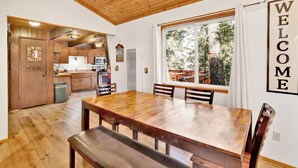 A wooden dining table with benches, a kitchen with wooden cabinets, and a large window with a view of trees.