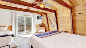 A wooden cabin bedroom with a bed, a ceiling fan, and a sliding glass door leading to an outdoor deck.