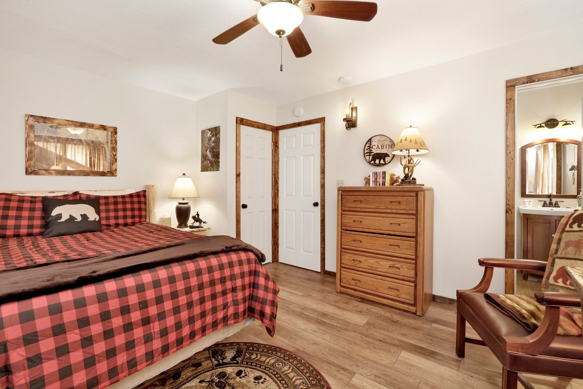 A bedroom with a bed, a dresser, a chair, a ceiling fan, and a wall-mounted lamp.