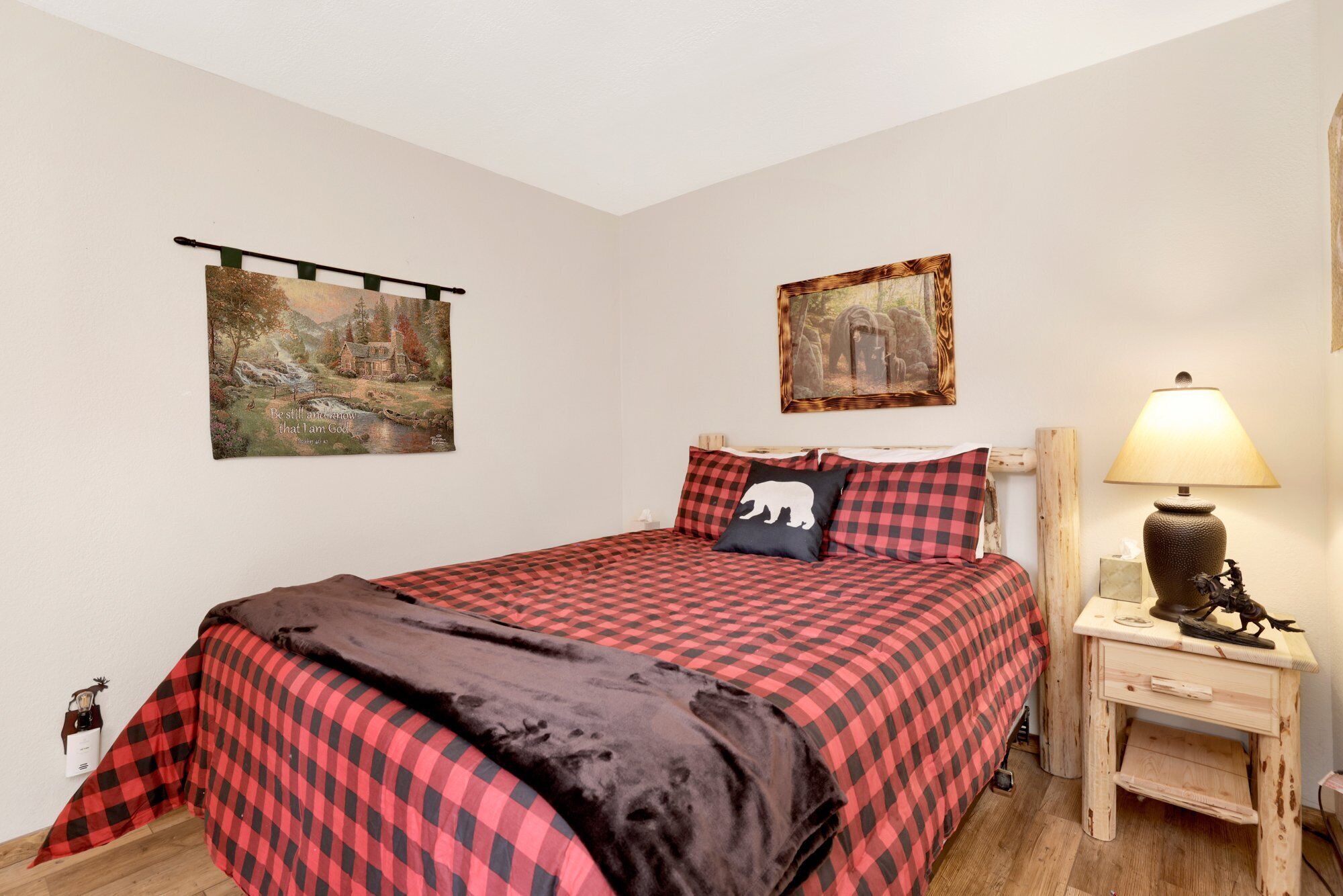 A bedroom with a bed, a nightstand, a lamp, and two paintings on the wall.