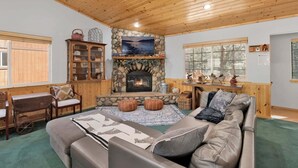 A cozy living room with a stone fireplace, wooden ceiling, and a large window.