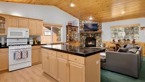 A cozy kitchen with wooden cabinets, a stone fireplace, and a large island.