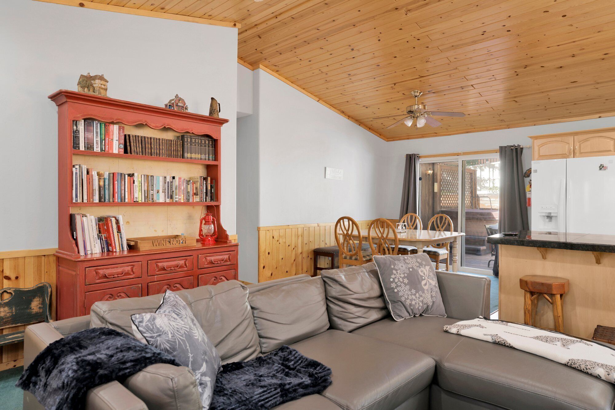 A cozy living room with a grey sectional sofa, a red bookshelf, and a wooden ceiling.