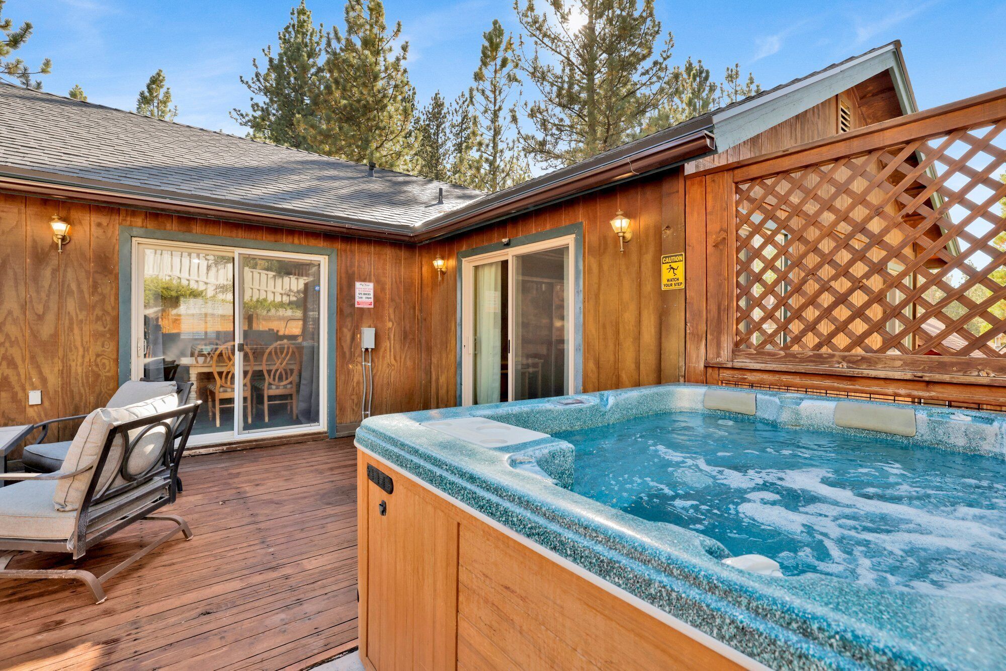 Een houten terras met een hottub, een overdekte patio en uitzicht op bomen.
