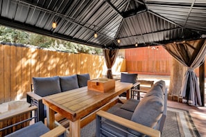 An outdoor patio with a wooden table and chairs, a cushioned bench, and a covered area with a metal roof.