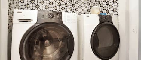 Two front-loading washing machines in a laundry area with patterned wallpaper.