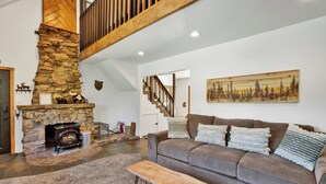 A cozy living room with a stone fireplace, a sofa with decorative pillows, and a wooden bench. - Maltby Modern LOG Cabin #2307 (Big Bear City)