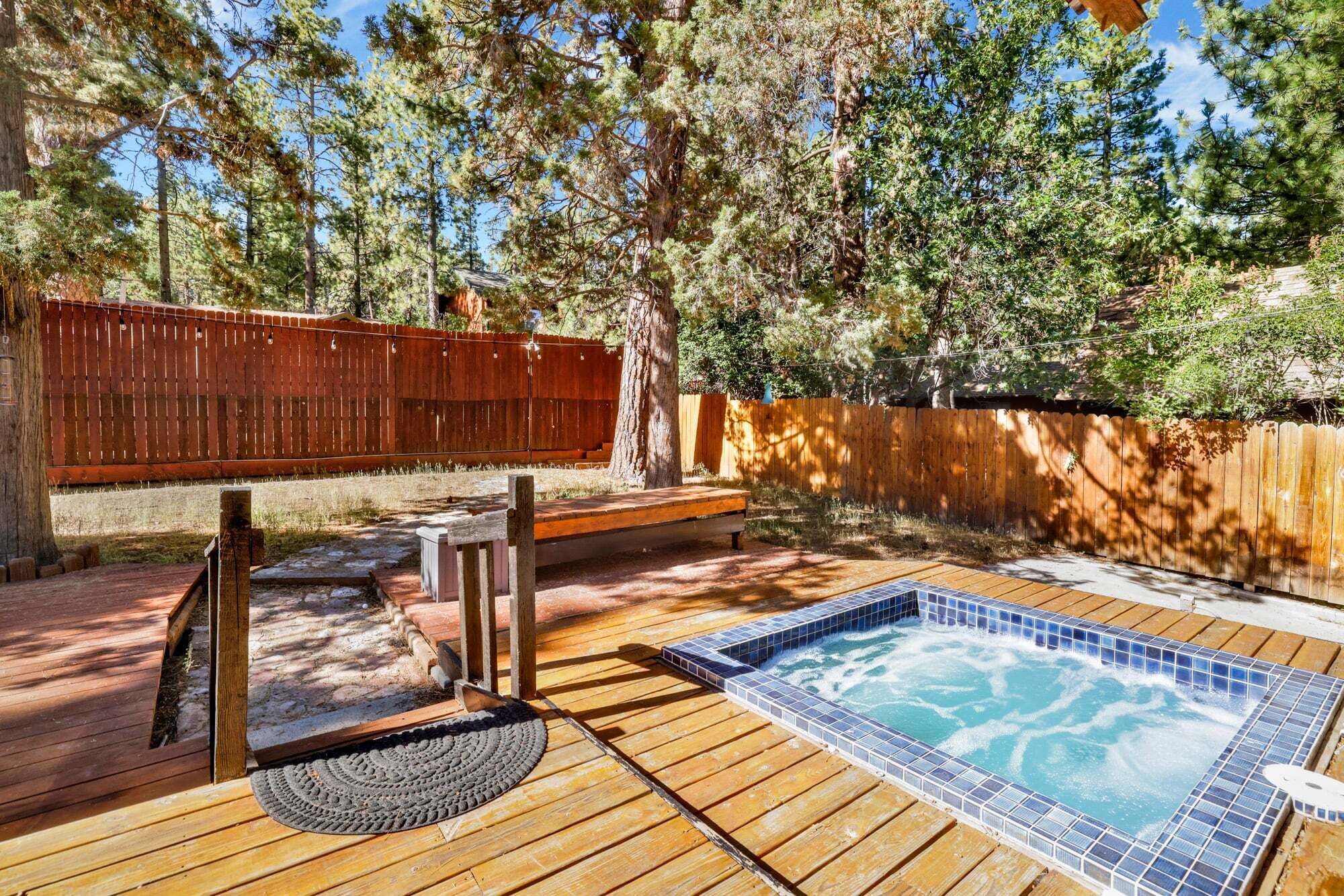 A wooden deck with a hot tub, a wooden bench, and a wooden fence.