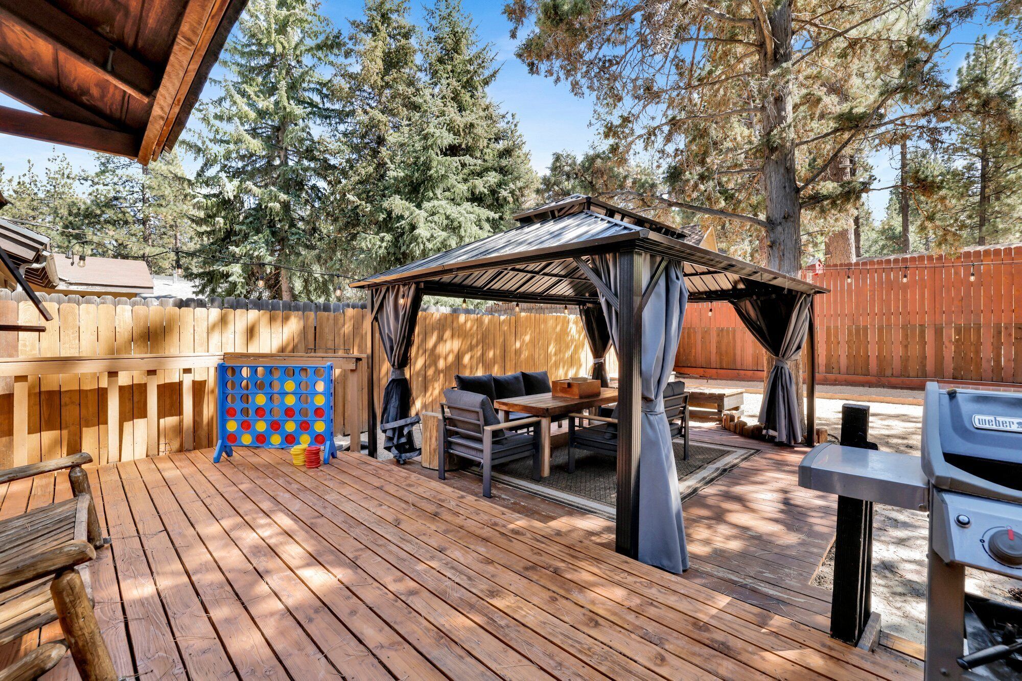 Une terrasse en bois avec un espace salon couvert, un barbecue et une clôture en bois.