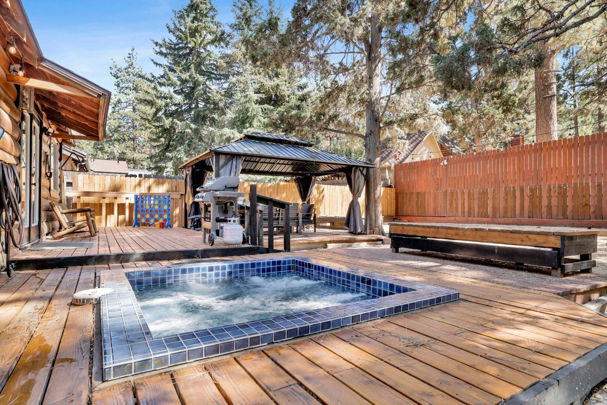 Una terraza de madera con un jacuzzi, una zona de estar cubierta y una valla de madera.
