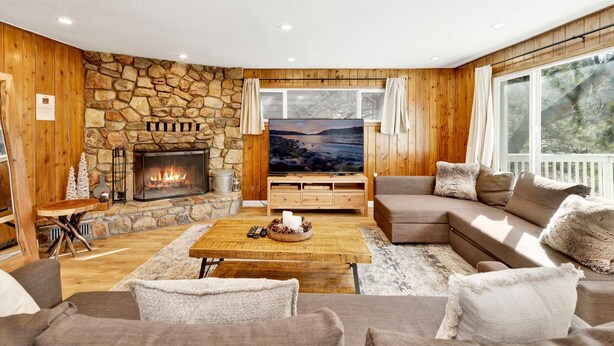 Ein gemütliches Wohnzimmer mit Kamin aus Stein, Holzwänden, einem großen Fernseher und einer bequemen Sitzecke.