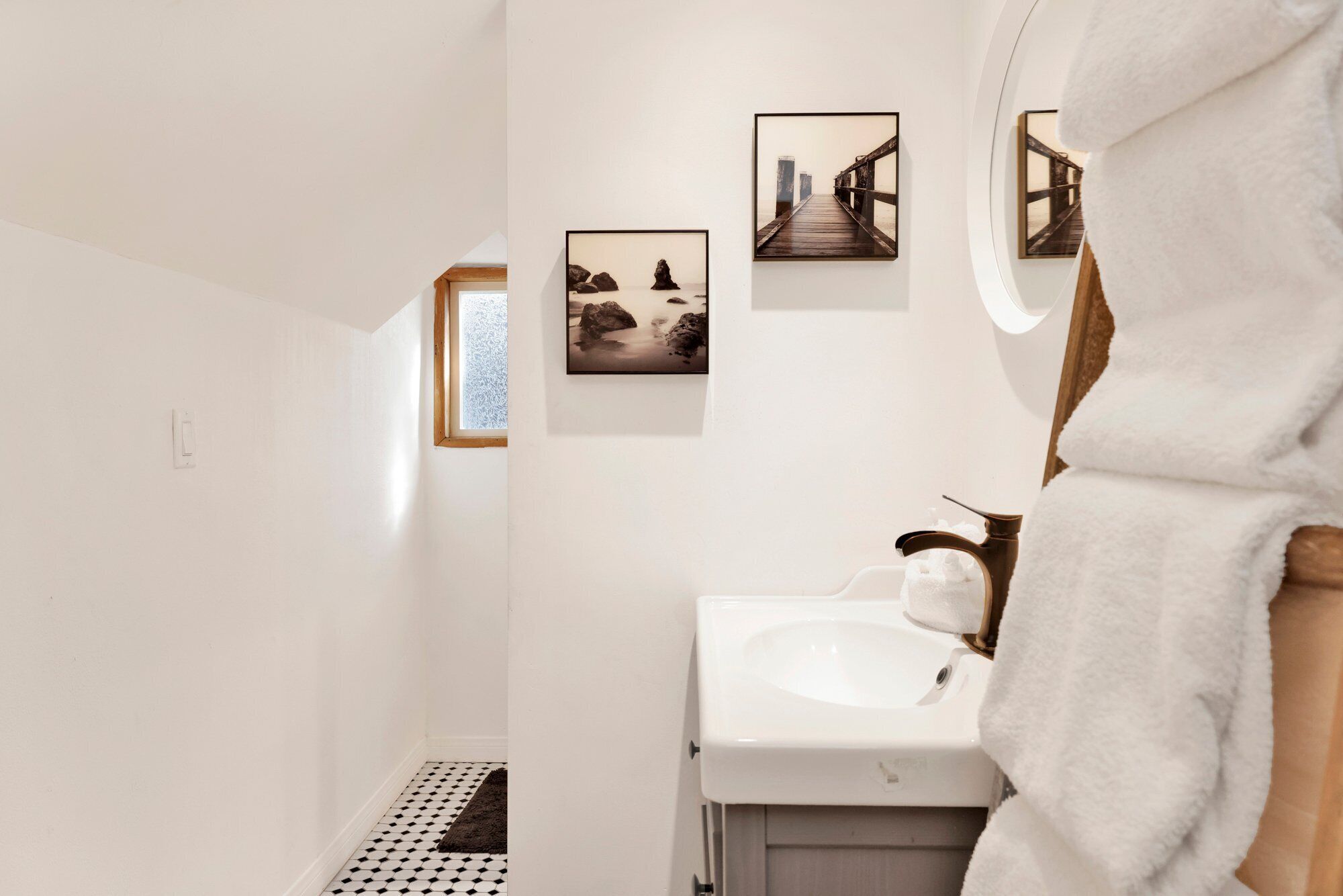A bathroom with a white sink, a towel, and three framed pictures on the wall.