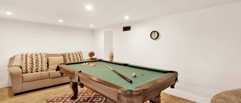 A pool table in a room with a sofa and a clock on the wall.