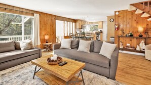 Ein gemütliches Wohnzimmer mit einem grauen Sofa, einem Holztisch und einem Essbereich mit Holzschränken und einer Küche im Hintergrund.
