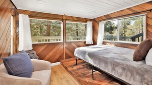 Ein Schlafzimmer mit Bett, einer Couch und großen Fenstern mit Blick auf Bäume.
