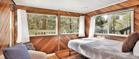 A bedroom with a bed, a sofa, and large windows offering a view of trees.
