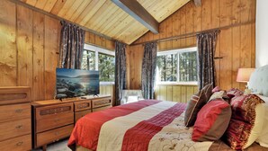 A wooden-paneled bedroom with a bed, dresser, TV, and windows.