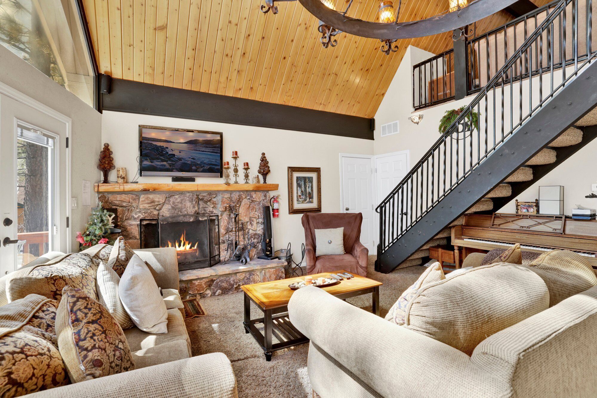 Un salon chaleureux avec une cheminée, des fauteuils confortables, un téléviseur et un escalier menant à l’étage supérieur.